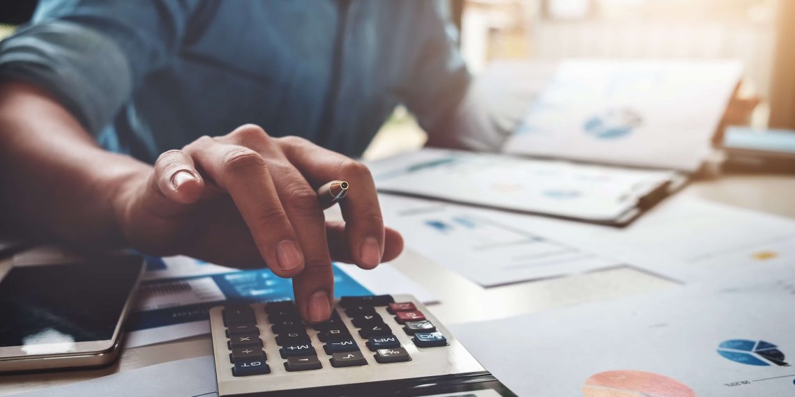businessman using calculator seated at a table with spreadsheets