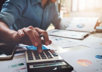 businessman using calculator seated at a table with spreadsheets